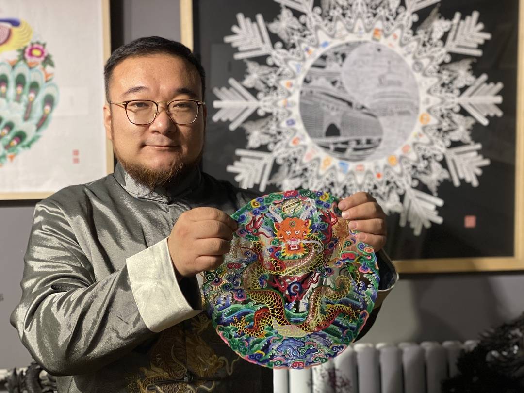 蔚县剪纸非遗传承人周利伟在展示剪纸作品,背后是其创作的《大美冬奥